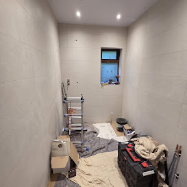 Bathroom wall tiling in progress with large light tiles