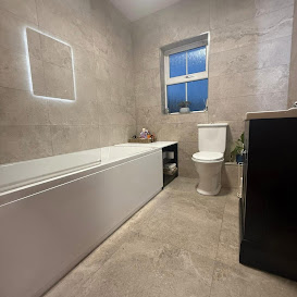 Bathroom with grey stone tiles, bath and illuminated mirror