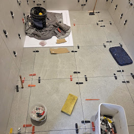 Bathroom floor tiling in progress with grey stone-effect tiles